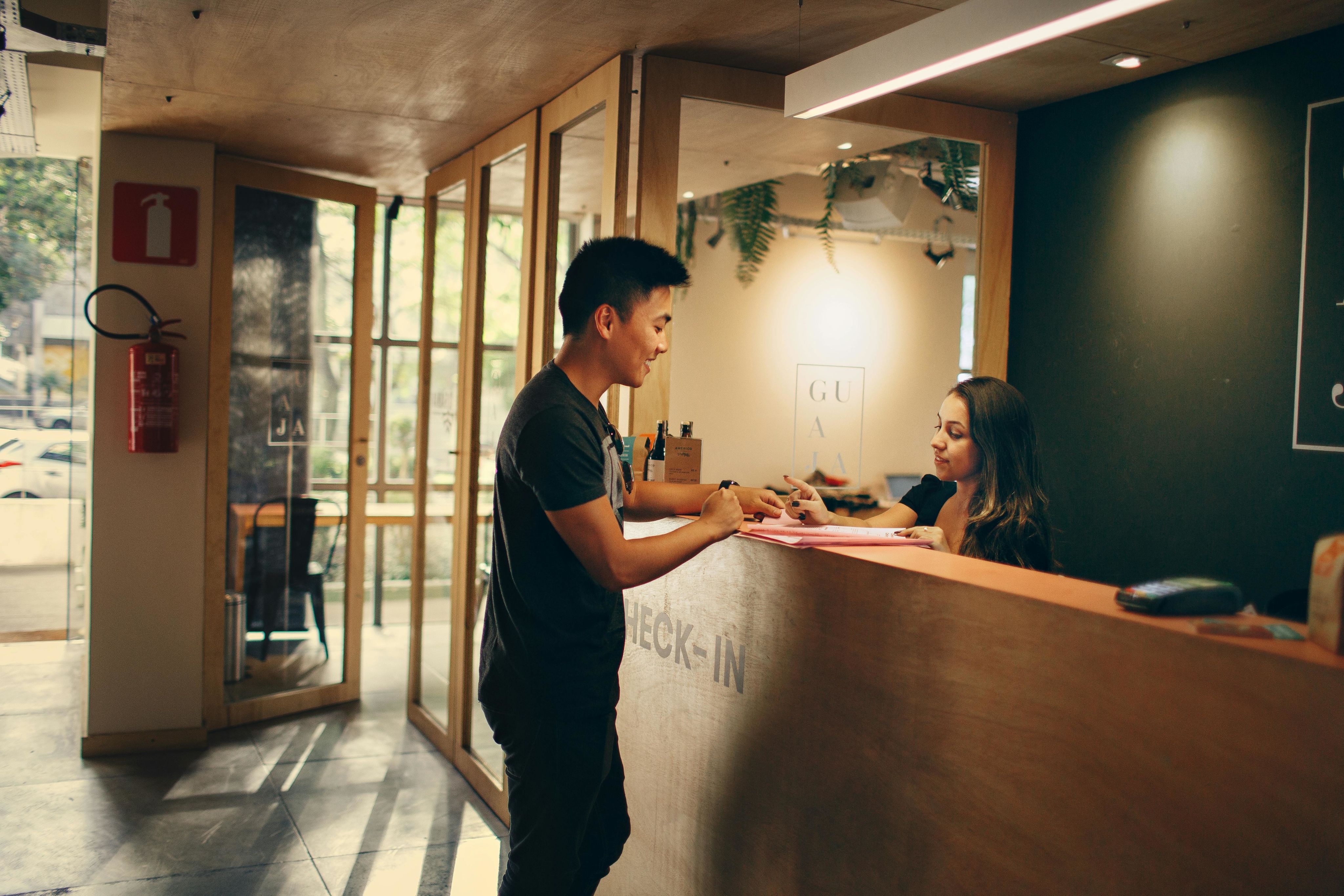 A customer checks in at a hotel reception d esk in Belo Horizonte, Brazil. Photo by Helena Lopes on Pexels