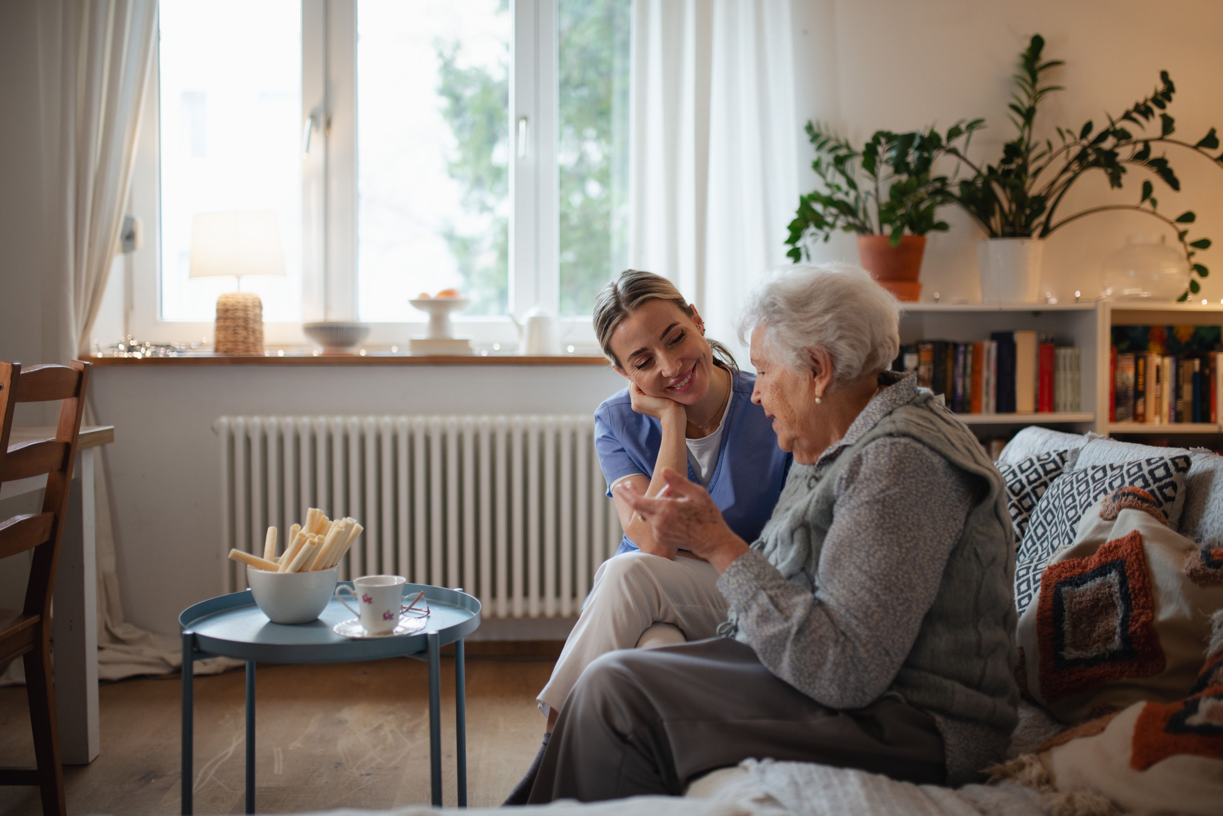 Caring healthcare worker visiting a senior patient at home, talking with her in living room. Copyright - Halfpoint / Adobe Stock