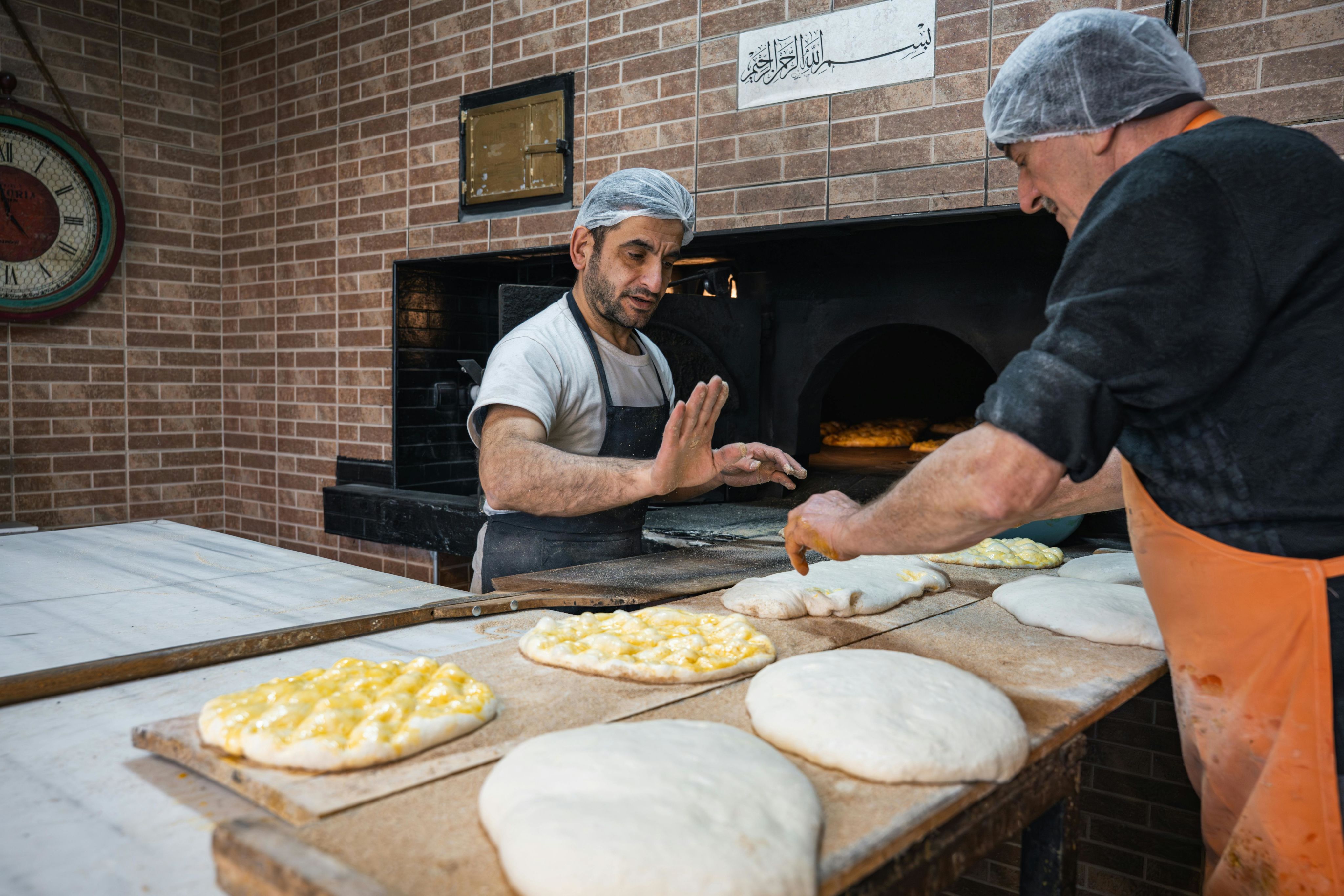 Two bakers making traditional flatbread in a stone oven, showcasing a classic bakery setting. Photo by Yasin Onuş on Pexels