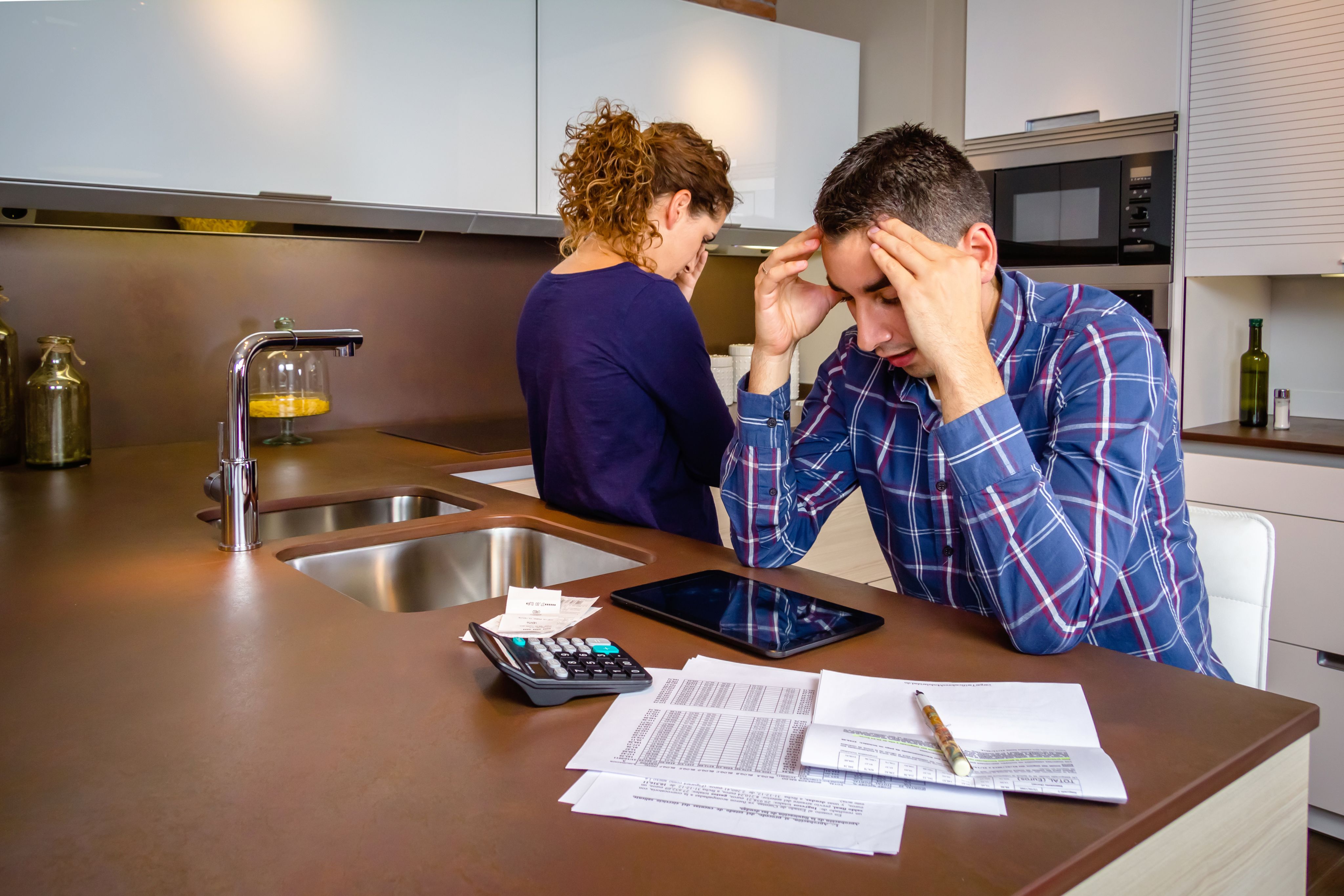 Stressed young couple with debts reviewing their bills at the kitchen counter - Copyright - JackF / Adobe Stock