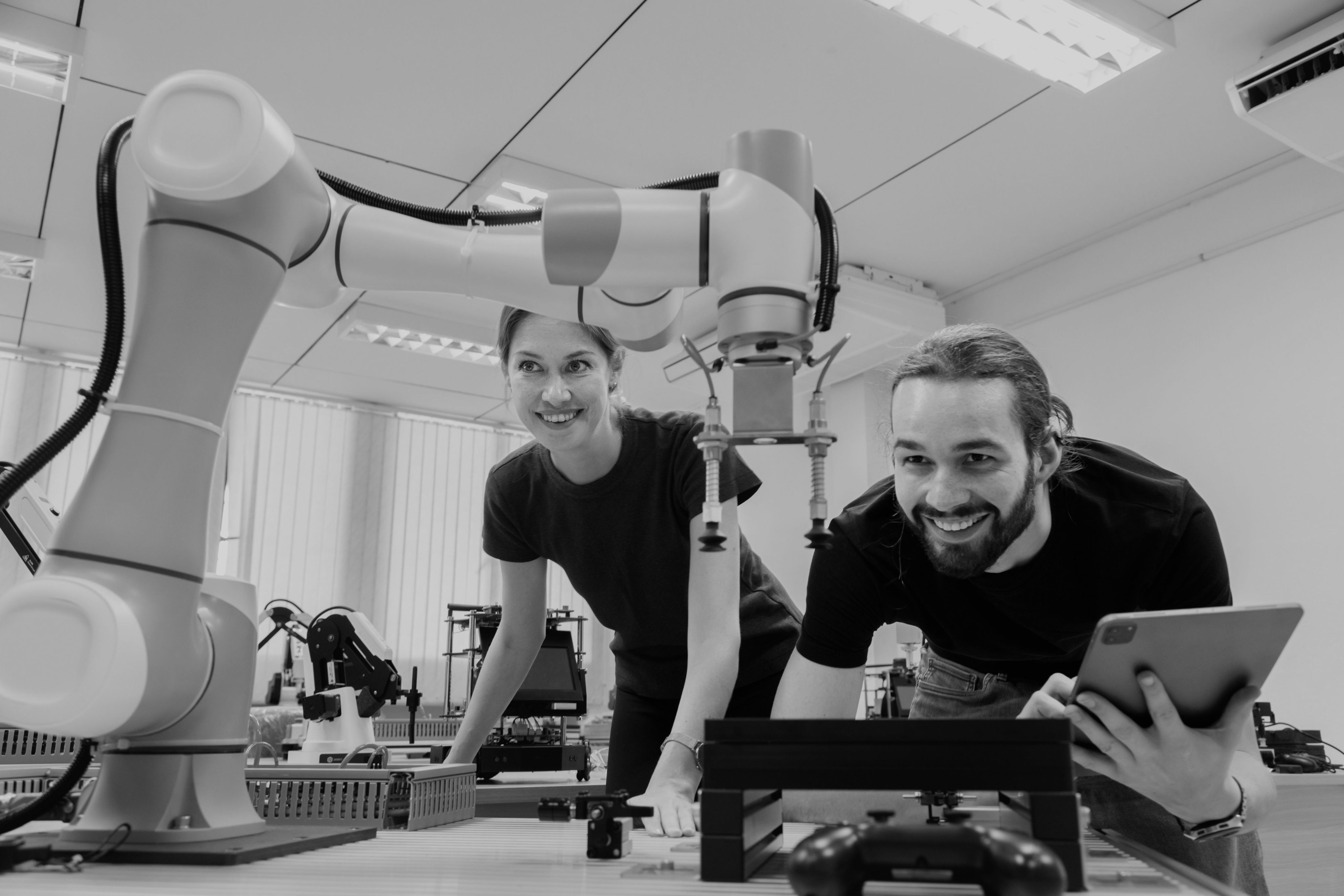 A man and a woman looking at a robotic arm with a laptop