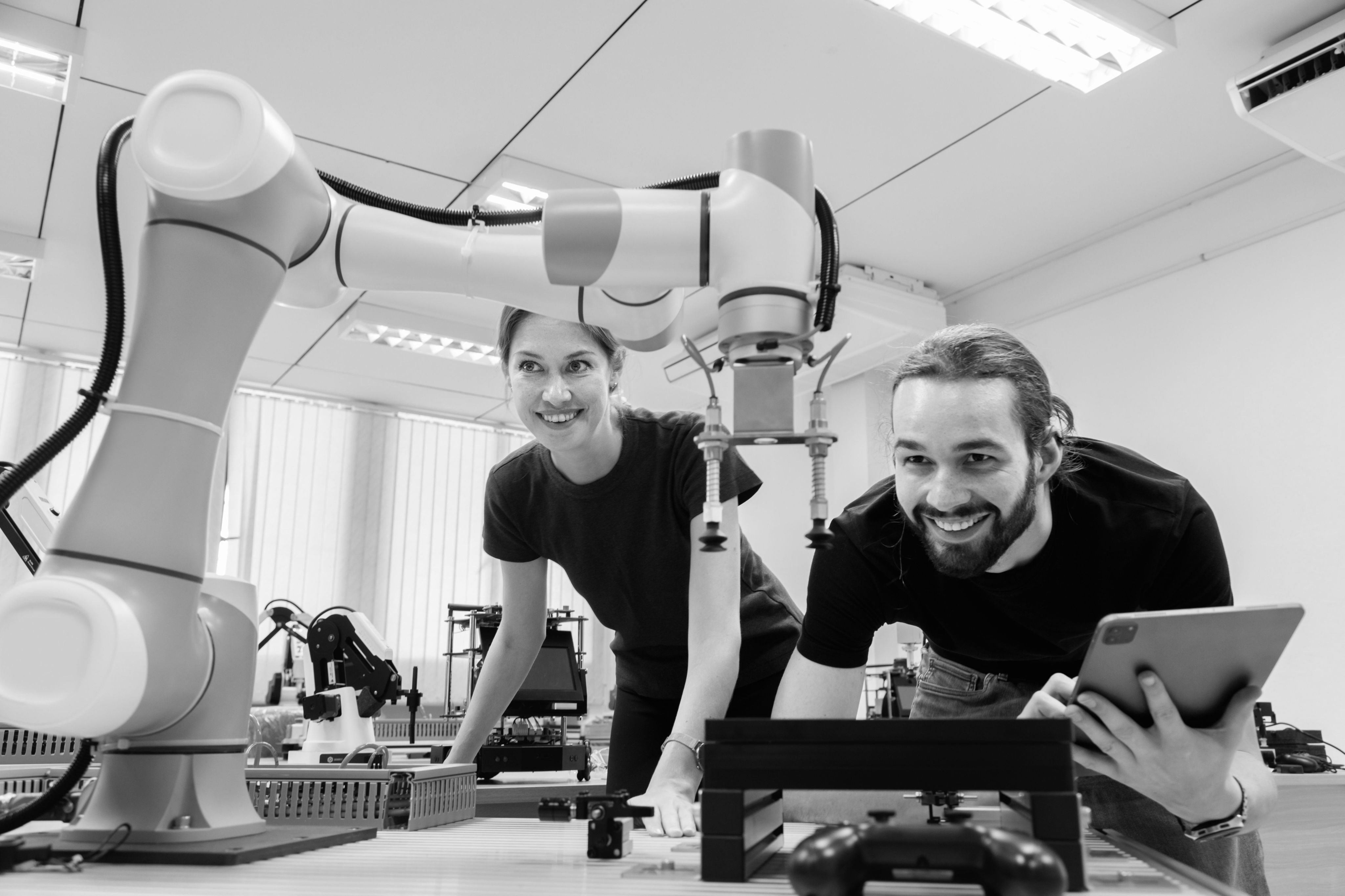 A man and a woman looking at a robotic arm with a laptop
