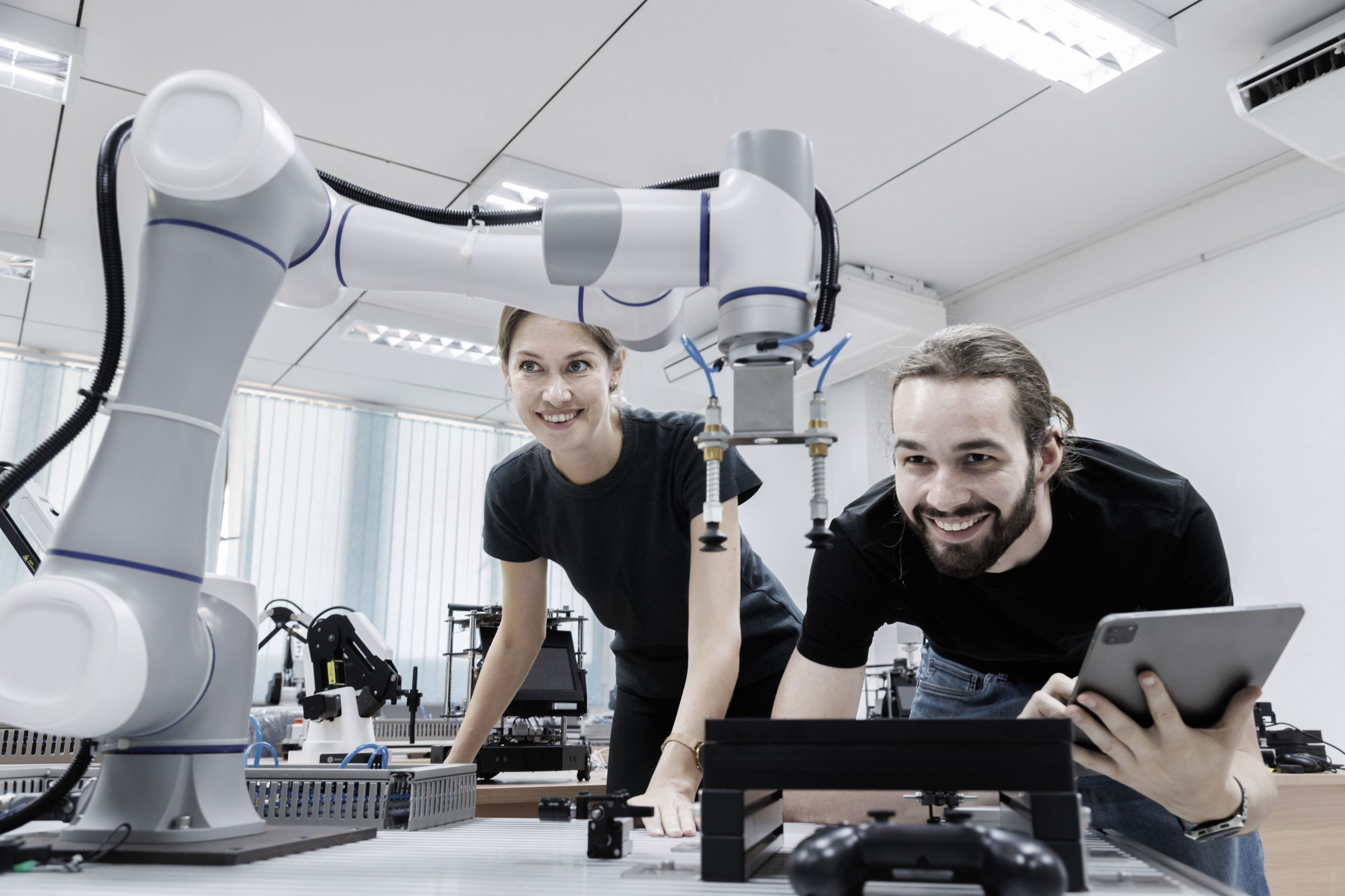 A man and a woman looking at a robotic arm with a laptop