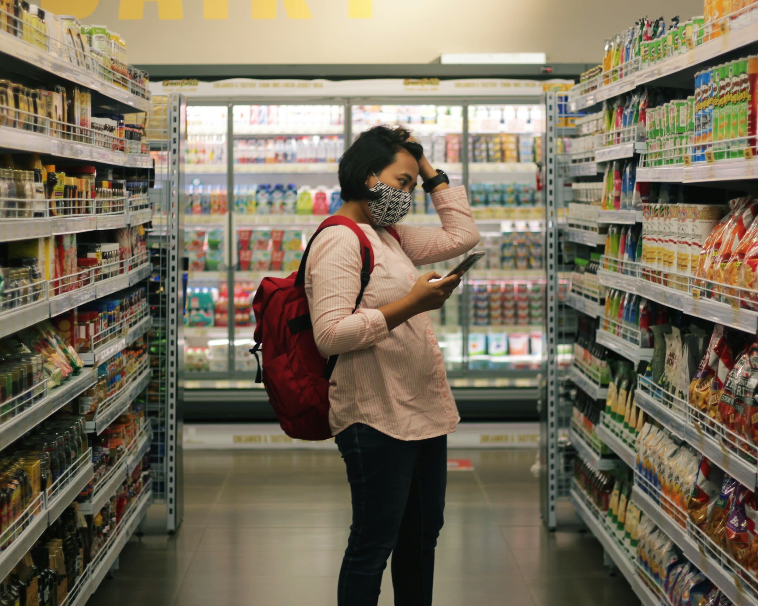 Woman wearing a mask in a supermarket looking at products in an aisle