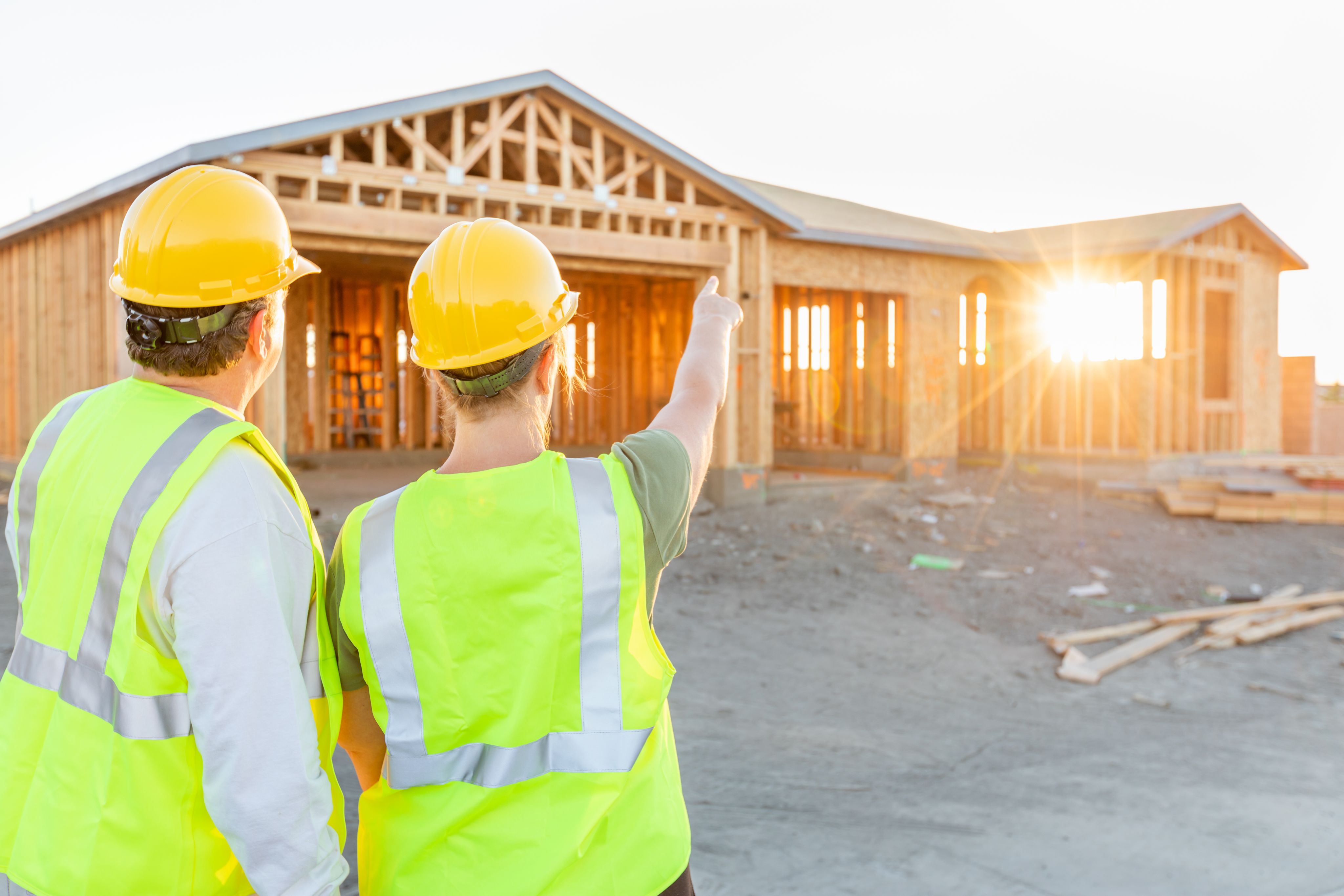 Two people looking at a house being built, wearing helmets and high visibility jackets