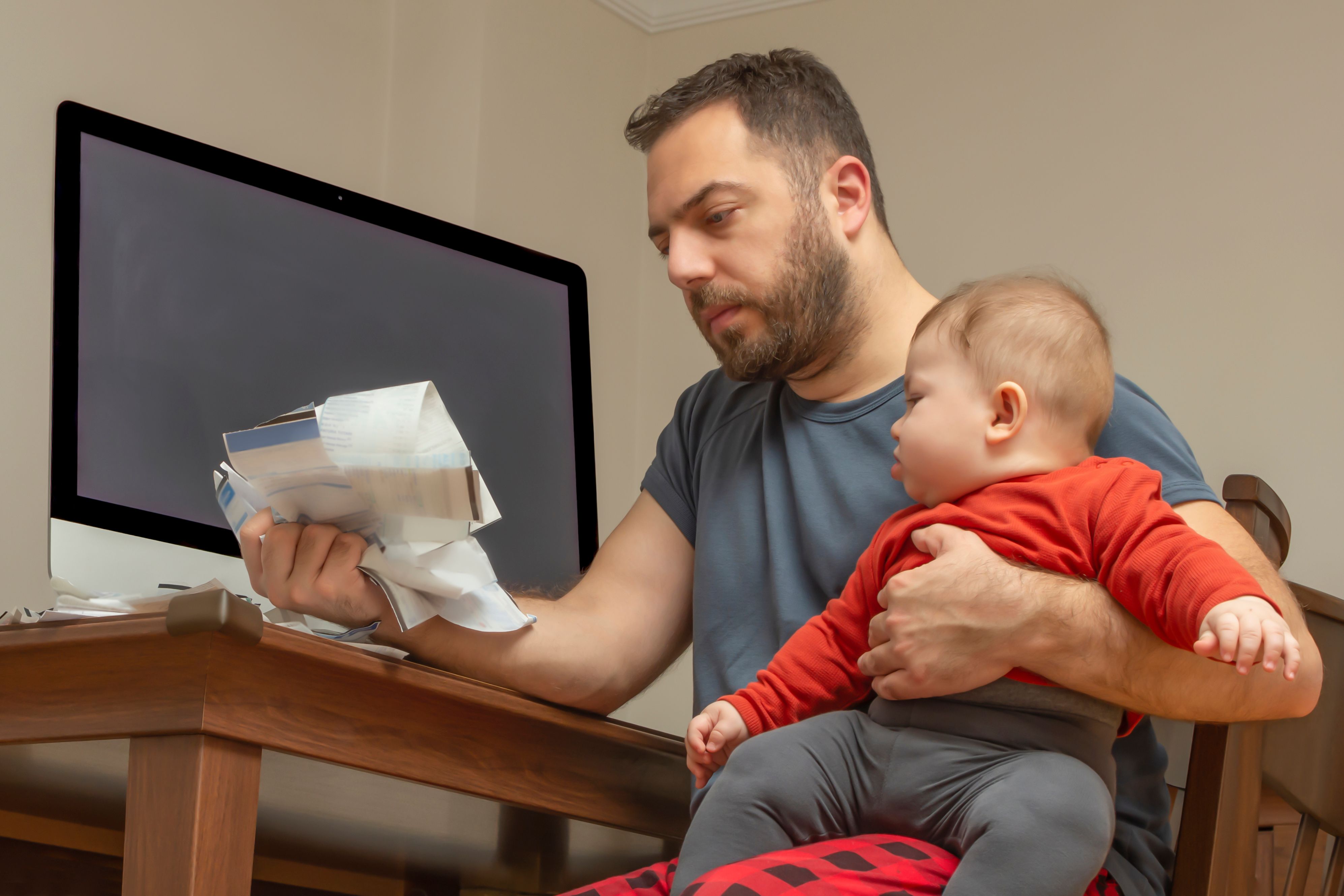 Man holding a baby looks at a bundle of invoices