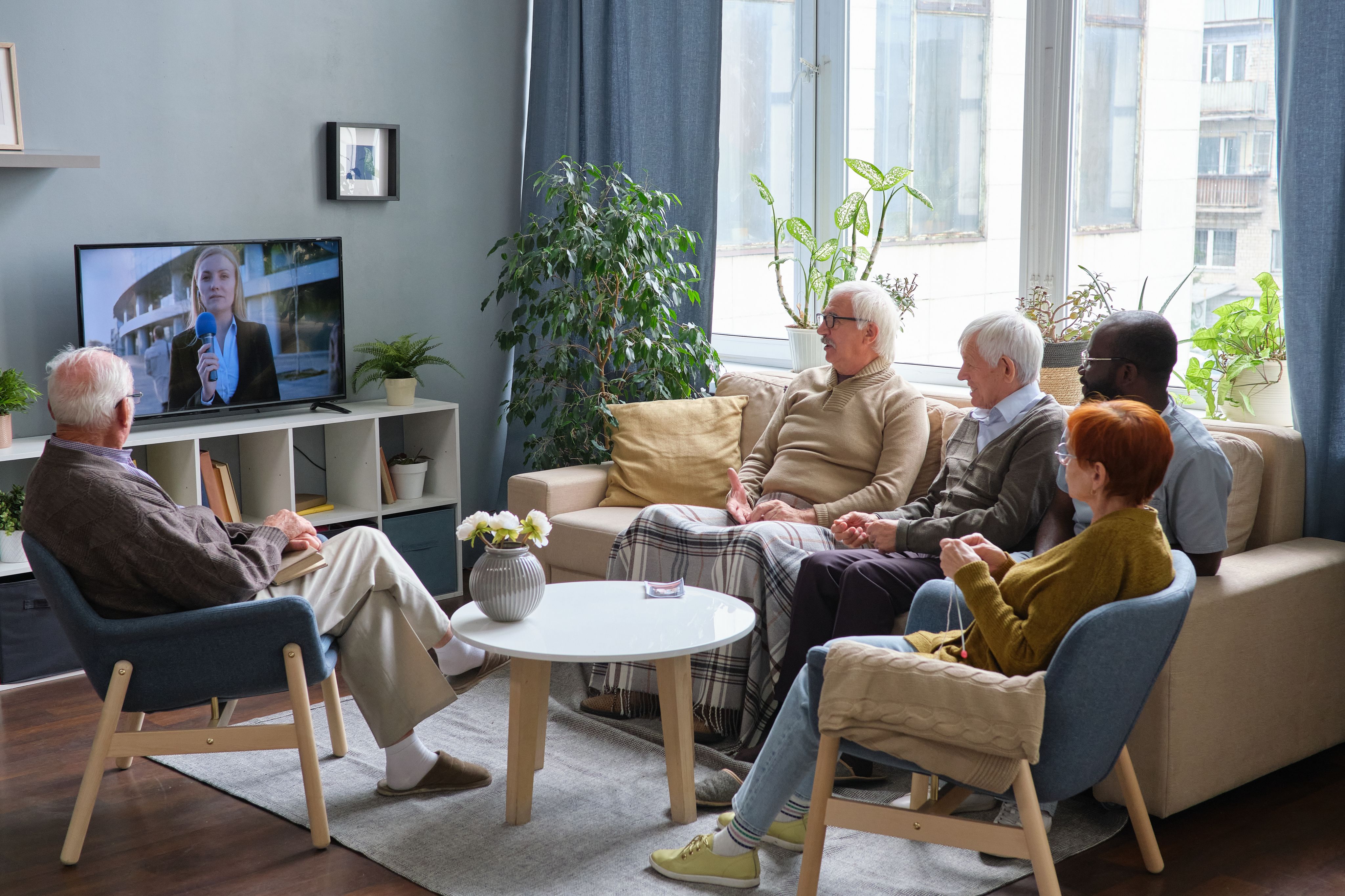 Group of senior people resting on sofa in the living room and watching news on TV together
